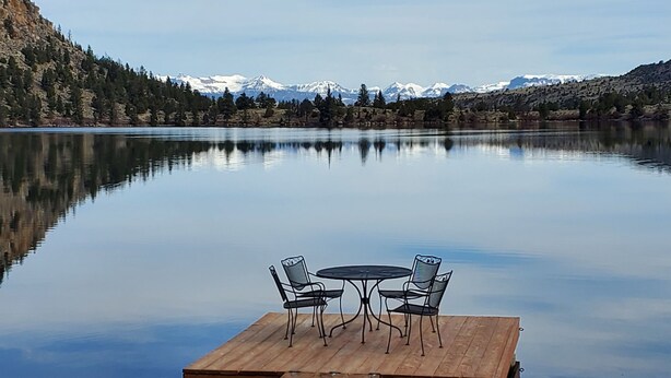 A wooden dock with two chairs and a table extending into a calm lake, surrounded by mountains and trees. - Beautiful lakeside retreat - Perfect for the adventuresome family -pet friendly (Dubois)