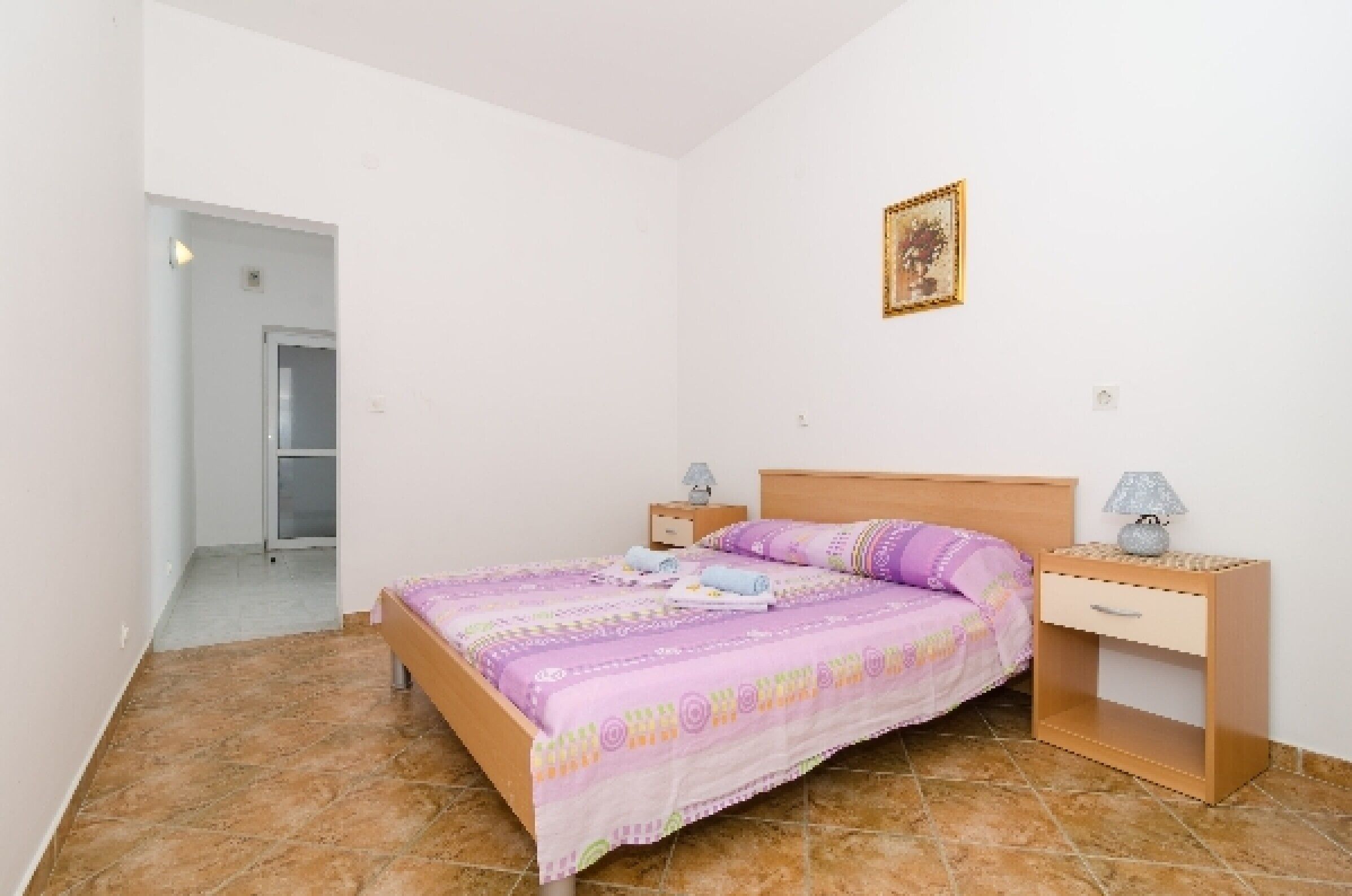 A bedroom with a bed, nightstands, a drawer, a door, and a wall-mounted picture.