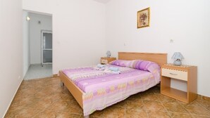 Un dormitorio con cama, mesitas de noche, un cajón, una puerta y un cuadro colgado en la pared.