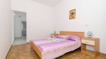A bedroom with a bed, nightstands, a drawer, a door, and a wall-mounted picture.