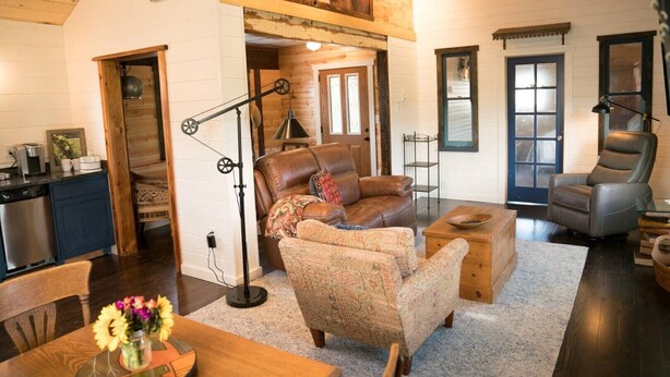 A cozy living room with a fireplace, leather sofas, and a dining area with a wooden table and chairs. - Charming well appointed Cottage in Ashland ( 800 + sq. ft. ) (Ashland)