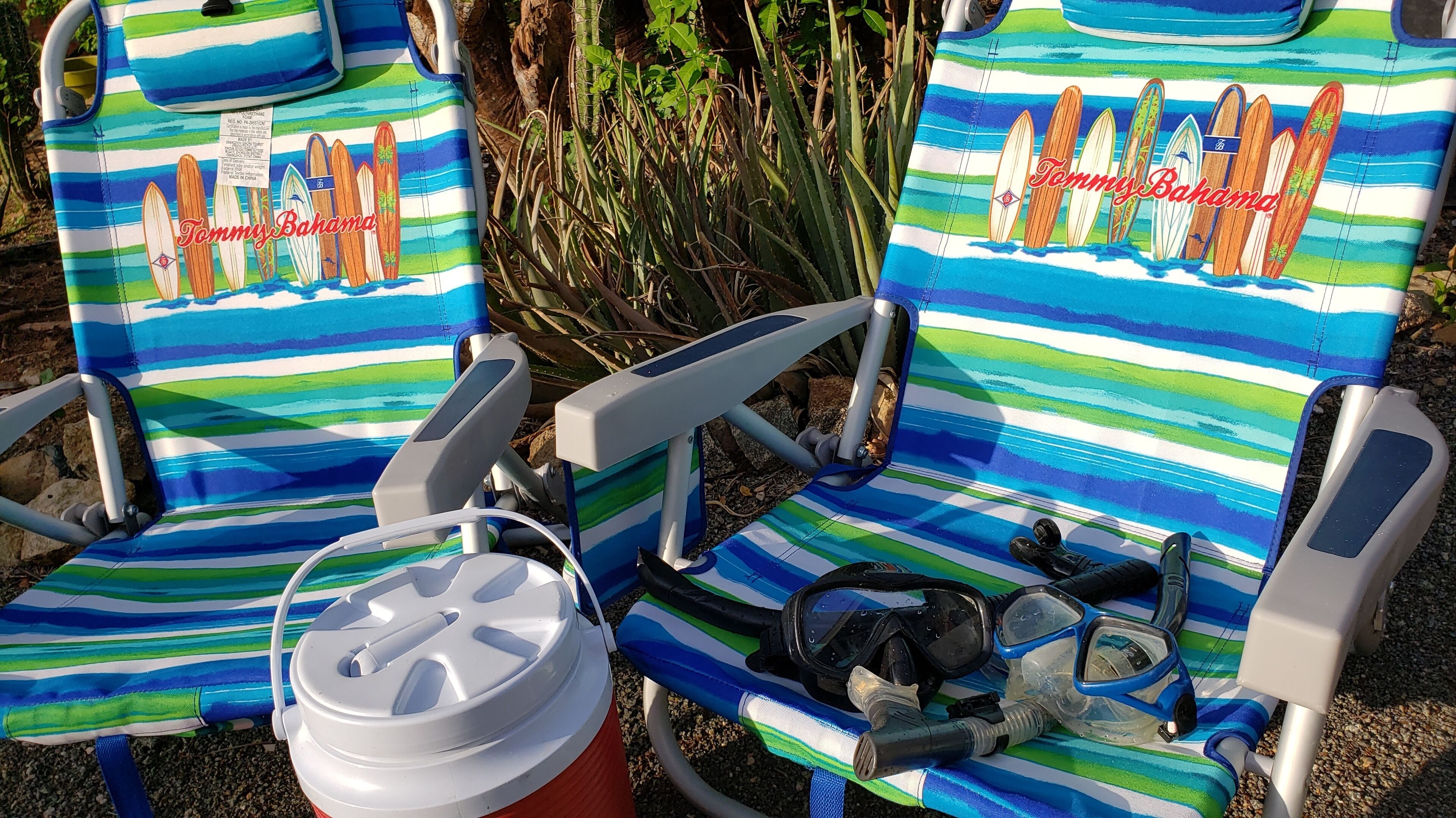 Dos sillas de playa con estampado a rayas y un logo, un cubo blanco y un par de máscaras de snorkel negras.