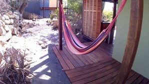A wooden deck with a hammock, a stone wall, and a building in the background. - A romantic stay and enjoy the nature! Aruba, Santa Cruz. (Santa Cruz)