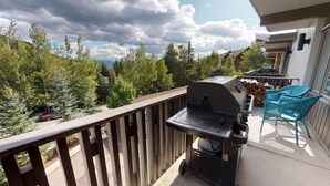 En balkong med en grill, stolar och utsikt över träd och berg.