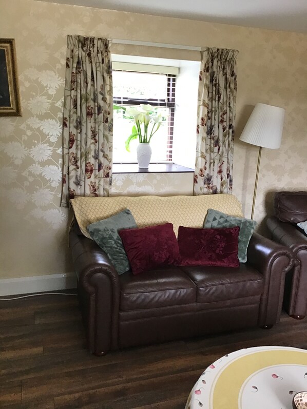 A living room with a brown leather sofa, floral curtains, a white vase with flowers, and a lamp. - Farmhouse in the Donegal Hills (Letterkenny)