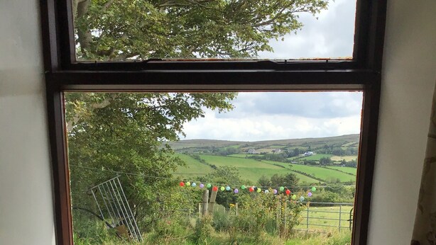 A window with a view of a rural landscape, a candle, and a potted plant. - Farmhouse in the Donegal Hills (Letterkenny)