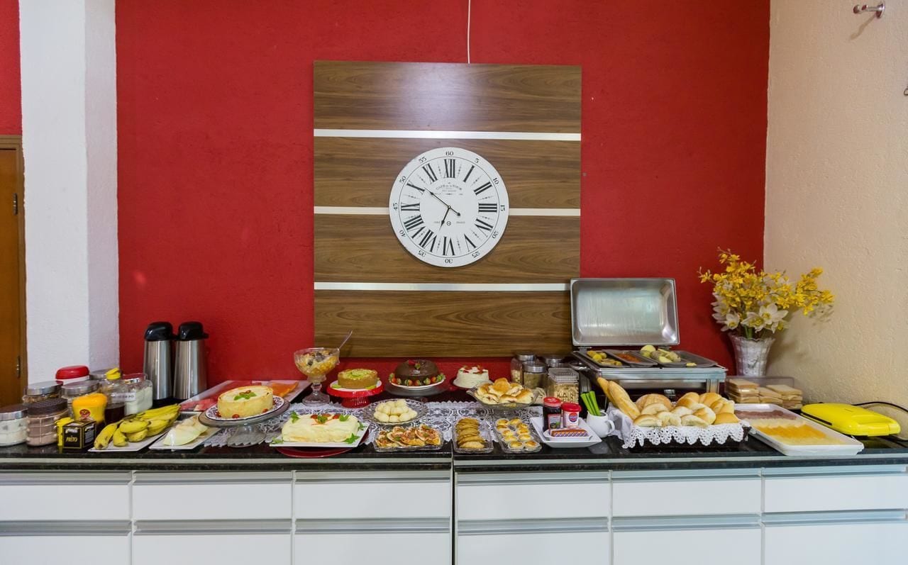 Disposición de un bufé con un reloj en la pared, diferentes alimentos, aderezos y un jarrón con flores.