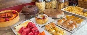 Un bufé con diversos postres y pastelería, incluyendo un pastel de chocolate, rosquillas y frutas cortadas.