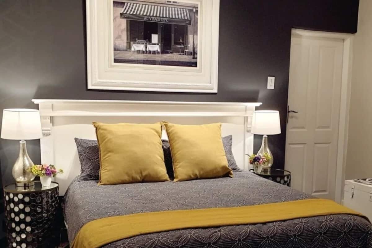 Une chambre à coucher avec un lit, deux tables de chevet, un tableau encadré au mur et une porte.