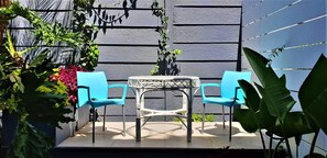An outdoor seating area with two blue chairs and a small round table, surrounded by various plants and a black wall. - Hadeda Hall (Johannesburg)