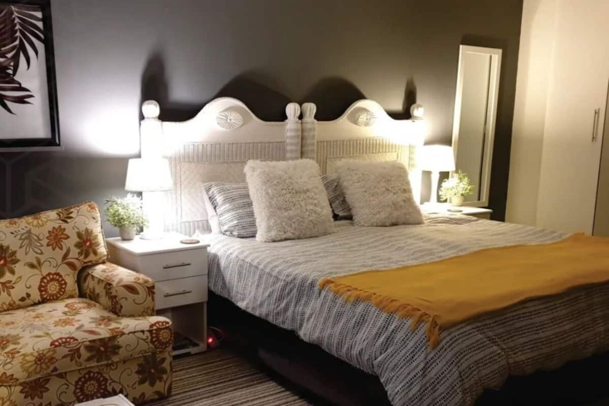 Une chambre à coucher avec un lit, des tables de chevet, une lampe, une chaise et un miroir.