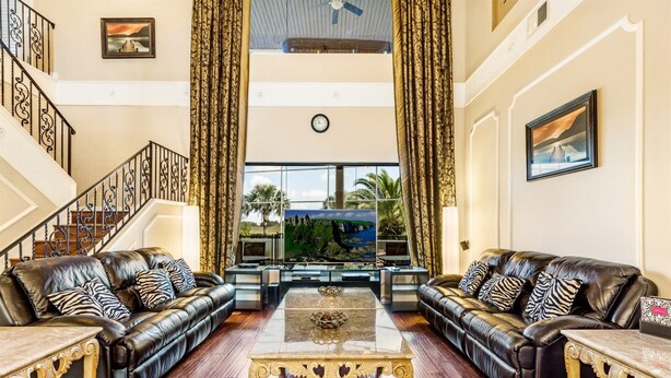 A spacious living room with leather sofas, a central coffee table, and a large window offering a view of palm trees. - Stunning Large 7 bed Home With Private Pool, Spa, Balcony, Cinema Room, Fitness Suite and Able to see the Disney Fireworks - 467 (Kissimmee)