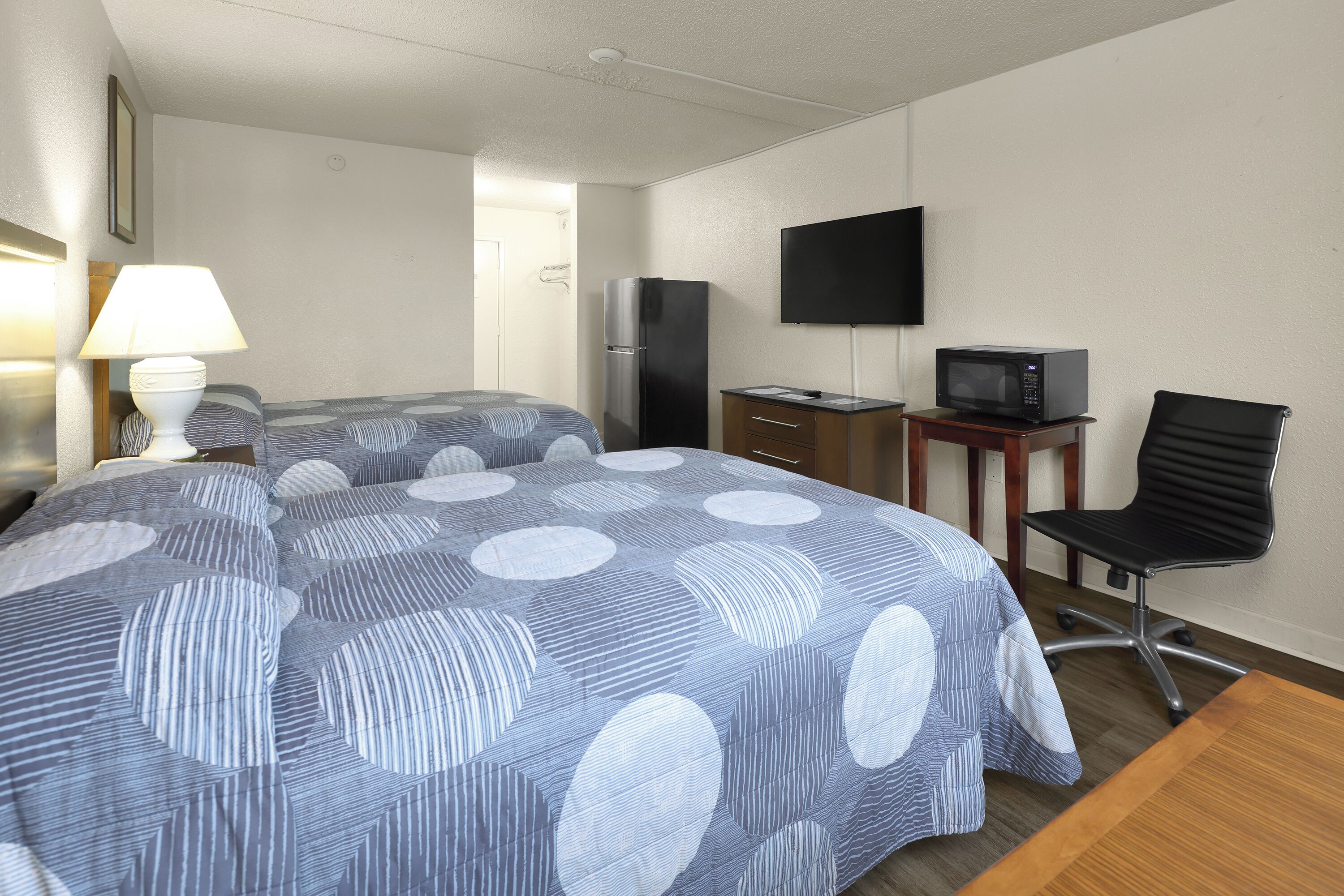 A hotel room with two beds, a desk with a television, a refrigerator, and a chair.