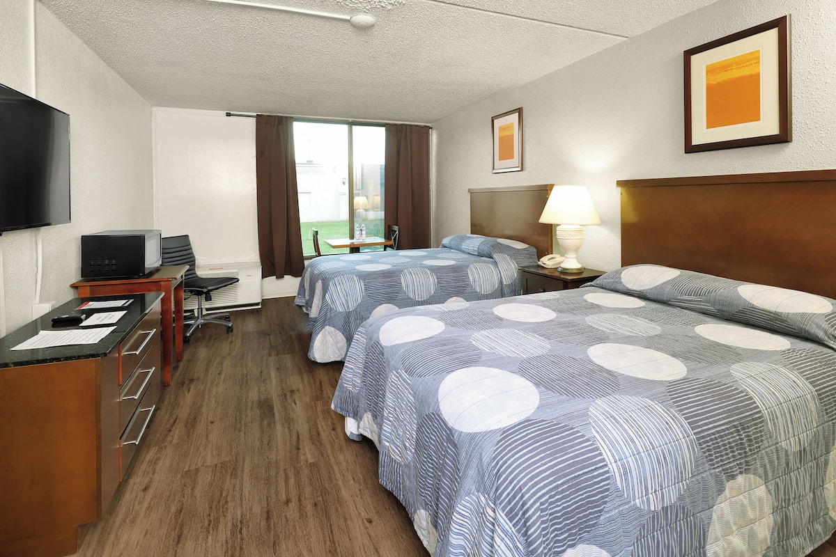 A hotel room with two beds, a desk, a chair, a TV, and a window with curtains.