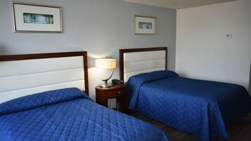 Una camera d'albergo con due letti, ciascuno con copripiumino azzurro trapuntato, un comodino con una lampada e quadri appesi alle pareti.
