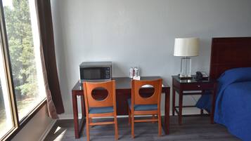 Ett hotellrum med ett skrivbord, två stolar, en mikrovågsugn, en lampa, en telefon och en säng med ett blått överdrag.