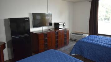 Ein Hotelzimmer mit Fernseher, Mikrowelle und einem Schminktisch. Es gibt zwei Betten mit blauer Bettwäsche.
