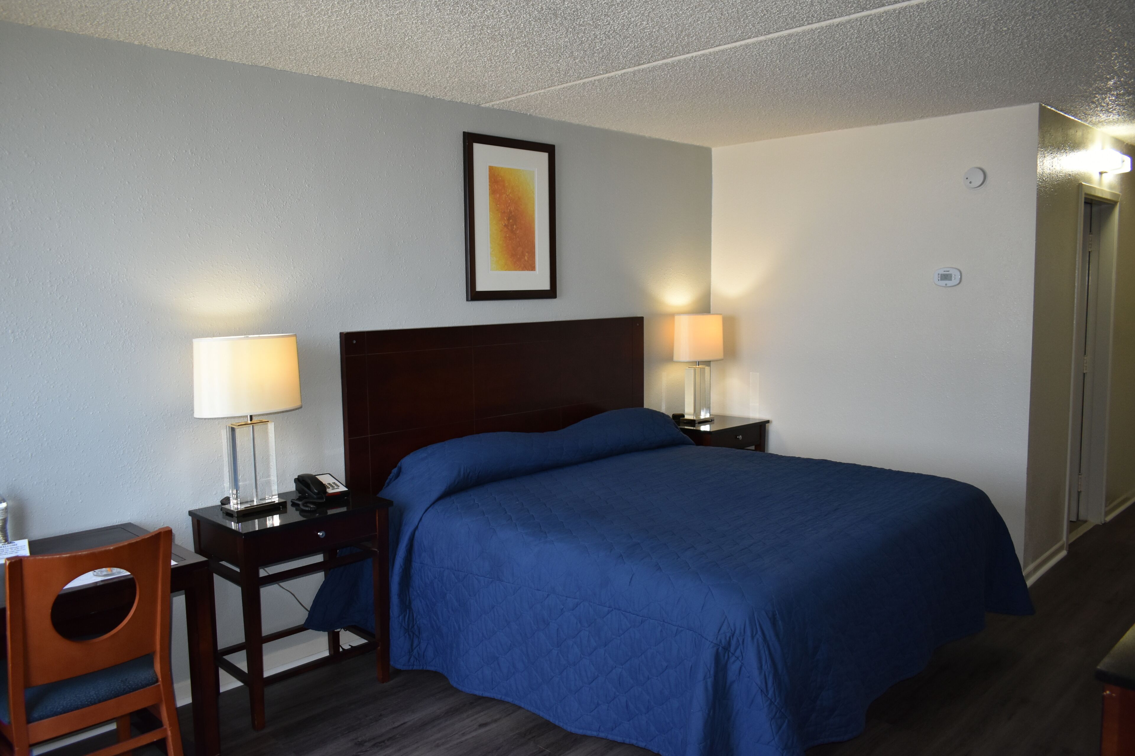 A hotel room with a large bed, two bedside tables with lamps, a desk with a chair, and a framed picture on the wall.