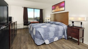 Ein Hotelzimmer mit einem großen Bett, einem Schreibtisch mit Stuhl, einem Fernseher und einem Fenster mit Vorhängen.