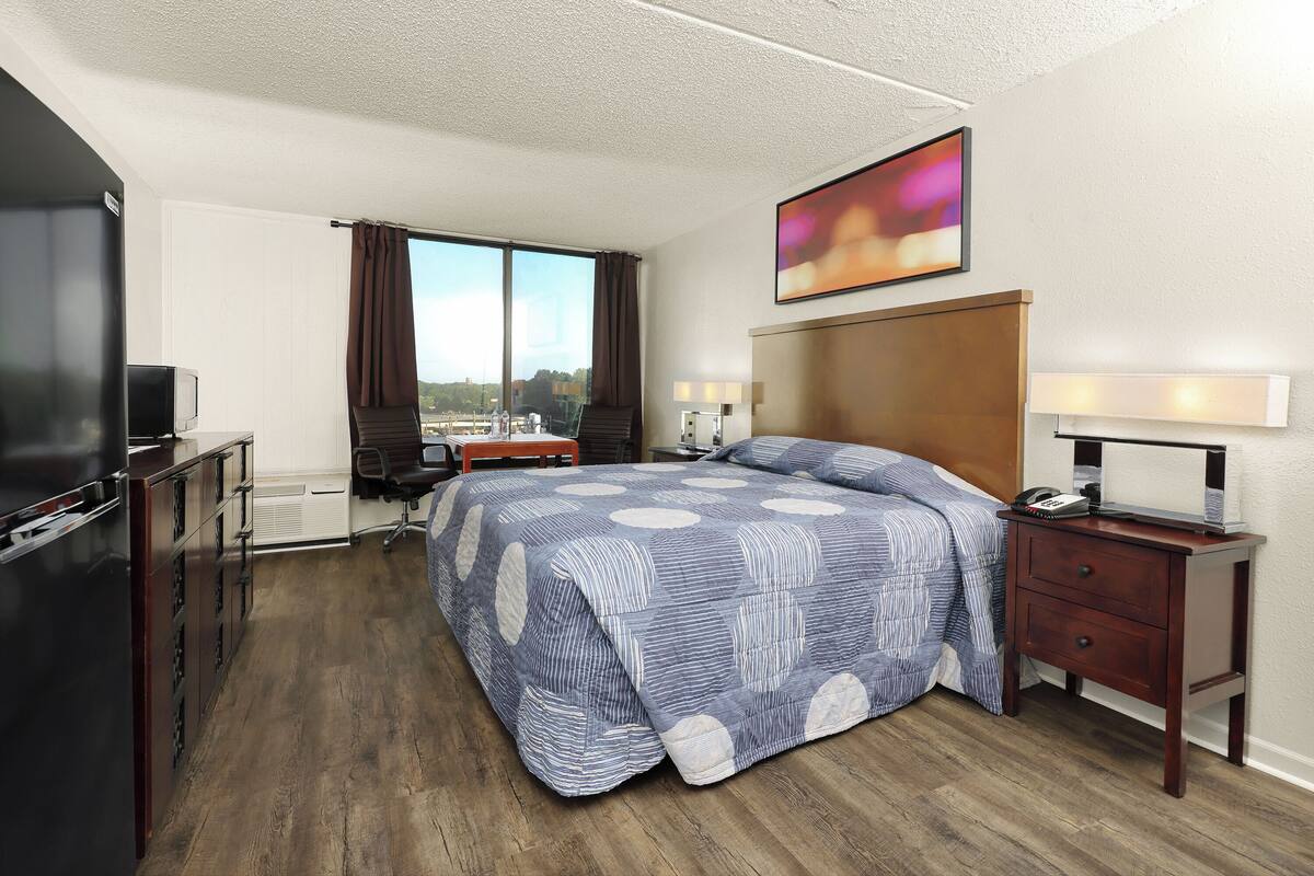 A hotel room with a large bed, a desk with a chair, a TV, and a window with curtains.
