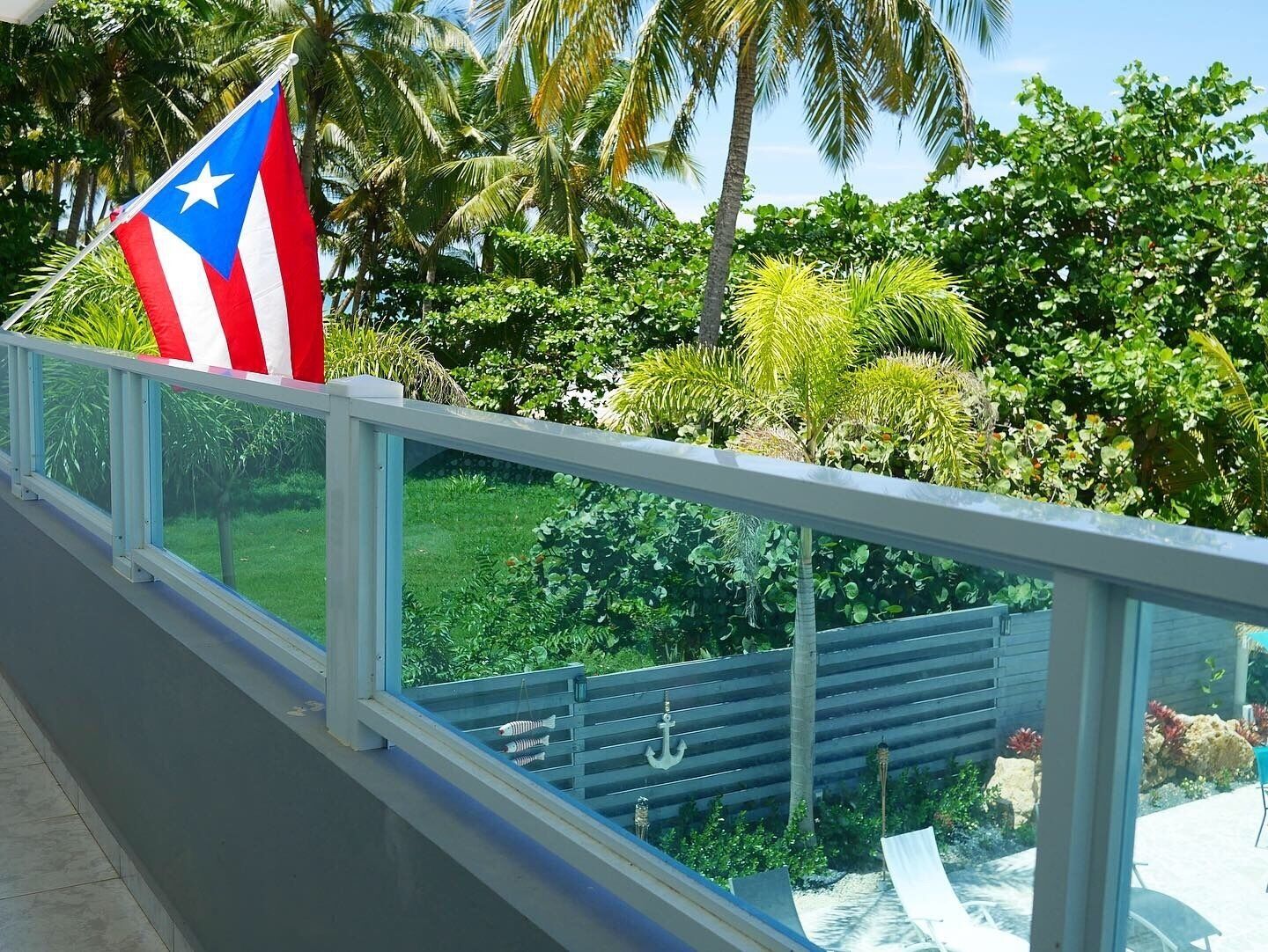 A balcony with a view of a lush garden, a flag, and a decorative anchor.