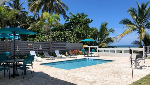 A pool area with lounge chairs, a table, and umbrellas. - Costa Paraíso Beach House (Aguada)