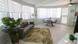 A modern living room with a gray sofa, a dining table with four chairs, and a large potted plant. - Costa Paraíso Beach House (Aguada)