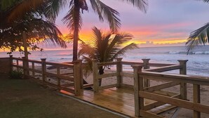 A wooden deck overlooking a beach with palm trees and a sunset. - Costa Paraíso Beach House (Aguada)