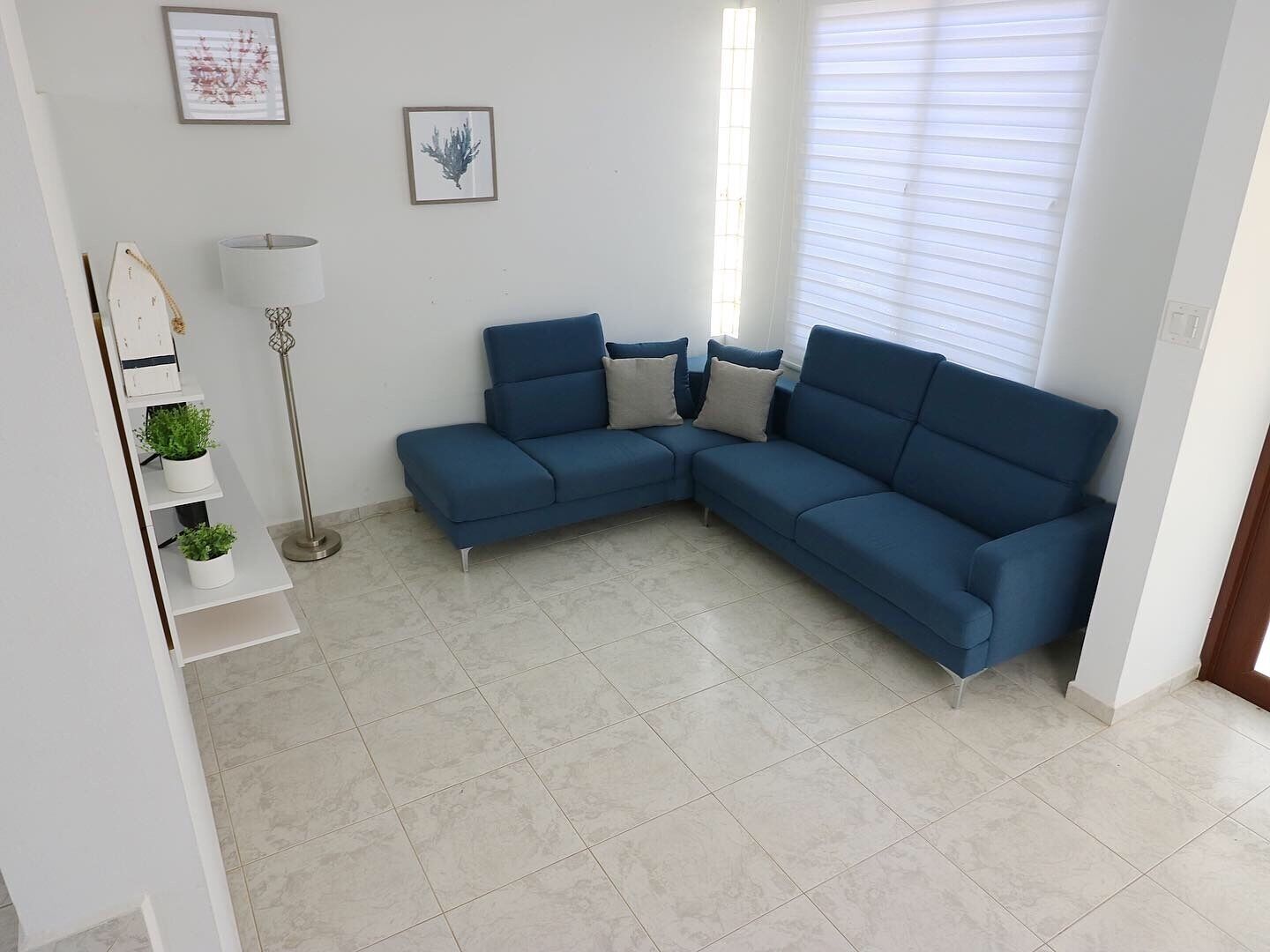 A living room with a blue sectional sofa, a floor lamp, and a white shelf with plants.