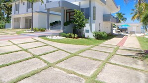 A modern two-story house with a covered patio, a well-maintained lawn, and a clear blue sky. - Costa Paraíso Beach House (Aguada)