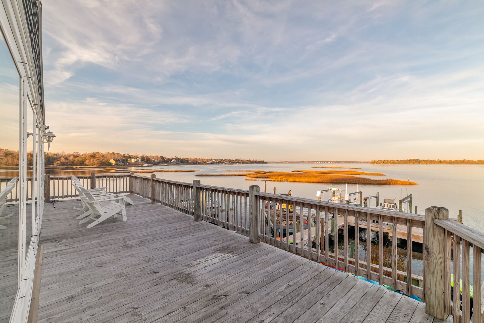 A wooden deck with a railing overlooking a calm body of water and a distant shoreline.