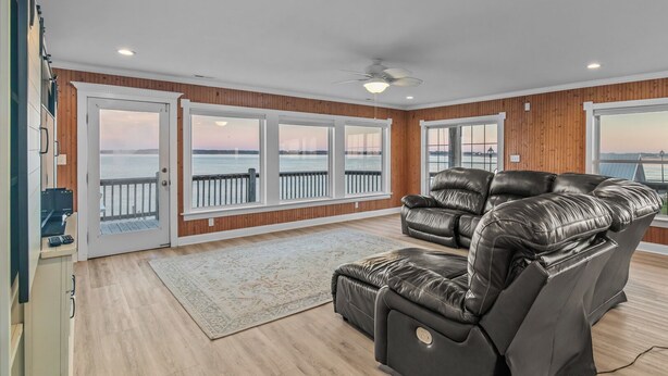 Ein geräumiges Zimmer mit einer großen Ledersofa, Holzboden und Blick auf das Wasser durch große Fenster.