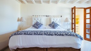 Una cama con una colcha blanca y azul estampada, dos almohadas decorativas y un cabecero de madera.