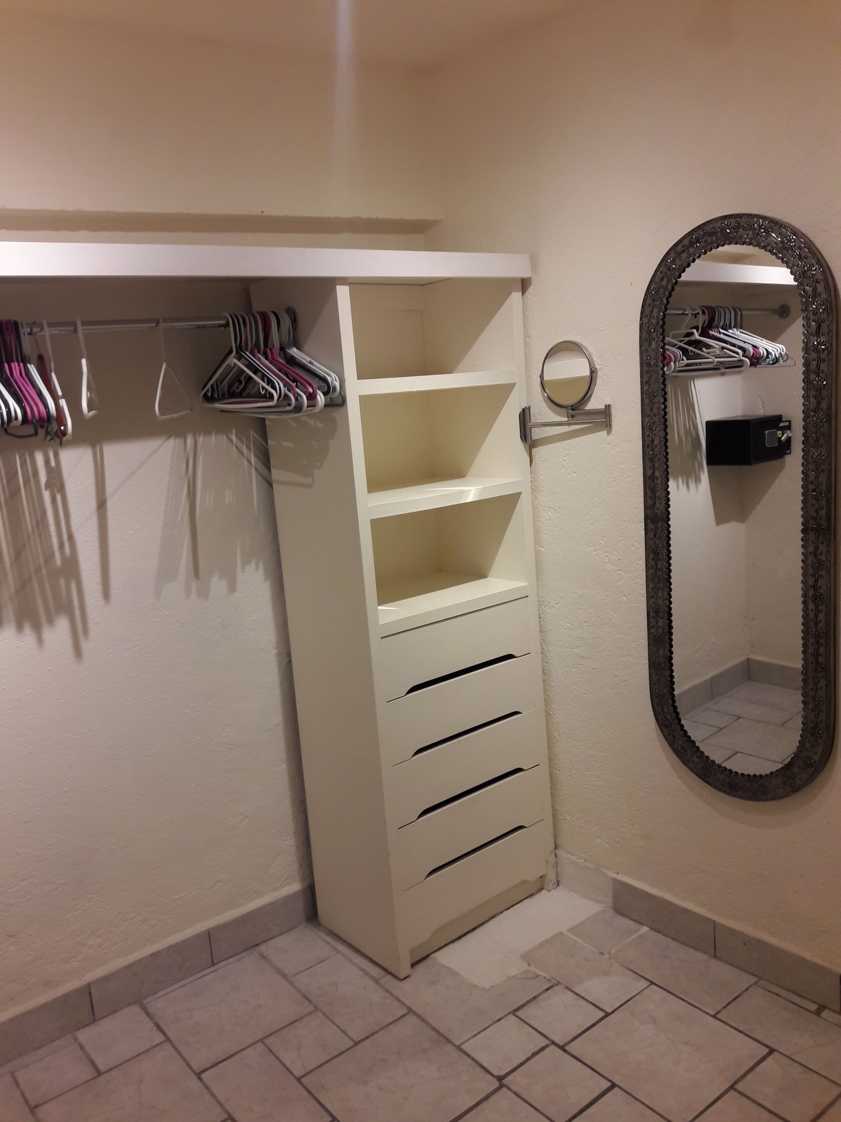 A closet with shelves and drawers, a hanging rack with clothes, and a mirror on the wall.