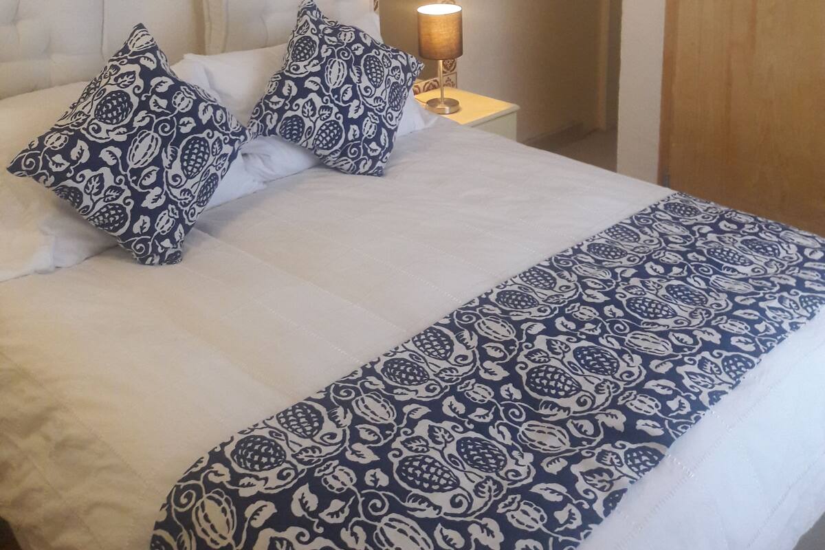 Un lit bien fait, agrémenté d’oreillers à motifs, une lampe de chevet et un miroir au mur.