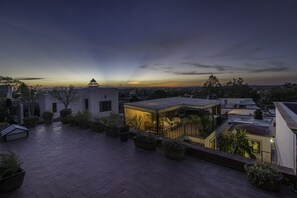 A rooftop terrace with potted plants, a seating area, and a view of the city skyline at dusk. - Pied-a-terre at Casitas Aparicio (San Miguel de Allende)
