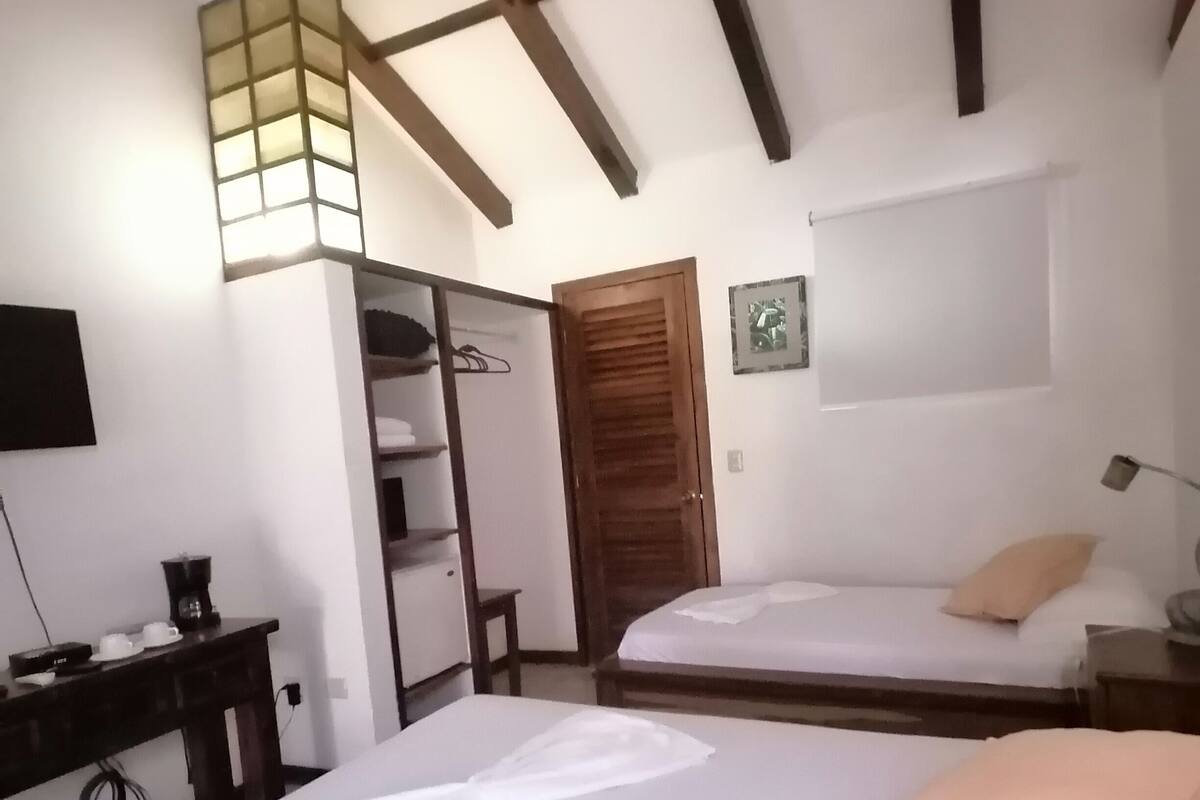 Un dormitorio con dos camas, un armario, un escritorio con lámpara y una lámpara de techo.
