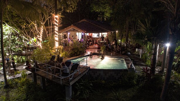 A pool area with a wooden deck, surrounded by tropical vegetation. - Hotel Nature Lodge Finca los Caballos (Cóbano)