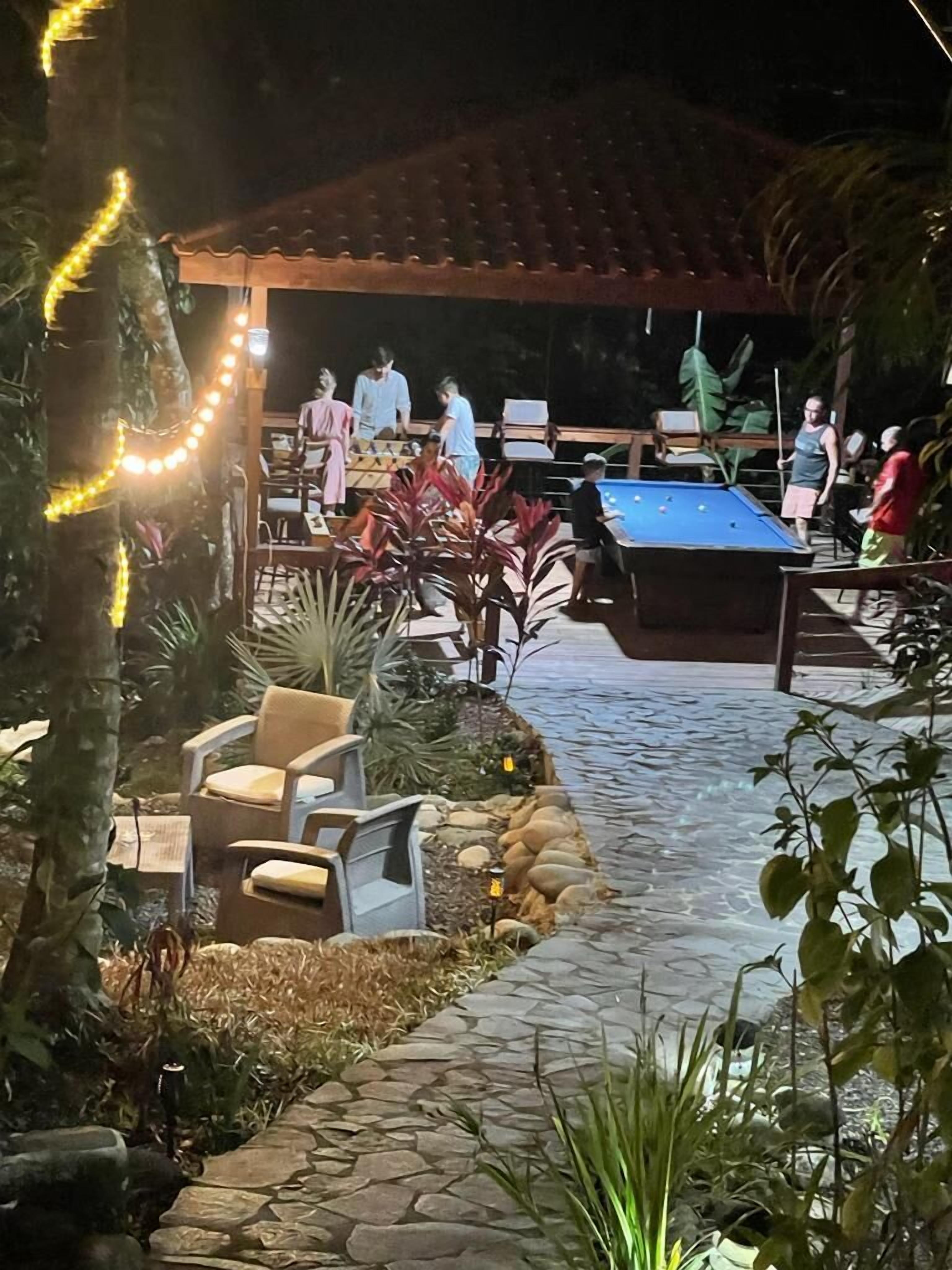 An outdoor pool area with a blue pool table, lounge chairs, and a covered seating area.