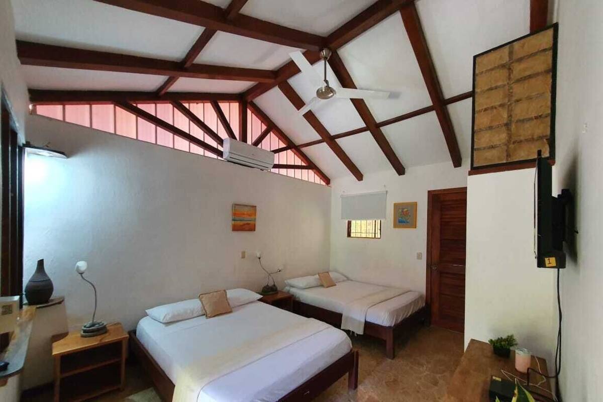 Un dormitorio con dos camas individuales, vigas de madera, un equipo de aire acondicionado, una mesita con una lámpara y una planta en maceta.