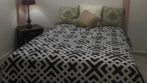 Una cama con una colcha estampada, una mesita de noche con una lámpara y dos almohadas decorativas.