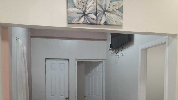 Una sala de estar con un sofá color beige, un televisor de pantalla plana montado en la pared y un cuadro sobre el sofá.