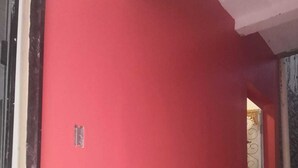 Pared exterior roja con una ventana y una puerta que dan a una zona con baldosas.