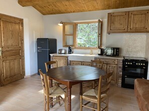 A kitchen with wooden cabinets, a black refrigerator, a stove, and a dining table with chairs. - AUTHENTIC BERGERIE (SOTTA)