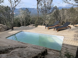 An outdoor swimming pool with wooden deck and lounge chairs, surrounded by trees and mountains in the background. - AUTHENTIC BERGERIE (SOTTA)