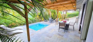 A pool area with a pergola, outdoor seating, and lush greenery.
