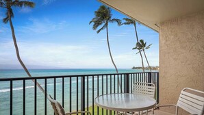 Uma varanda com vista para o oceano, palmeiras e uma mesa com cadeiras.