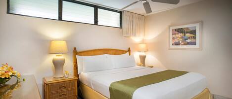 A hotel room with a bed, two bedside tables with lamps, a ceiling fan, a window with blinds, and a framed picture on the wall.
