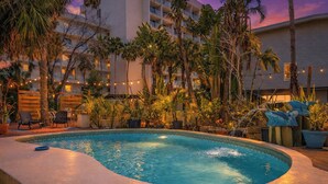 Una piscina de borde curvo, rodeada de plantas en macetas y mobiliario exterior.