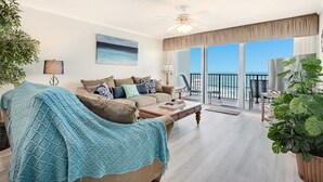 Ein geräumiges Wohnzimmer mit großem Fenster und Meerblick, Deckenventilator und einer gemütlichen Sitzecke mit Couchtisch.